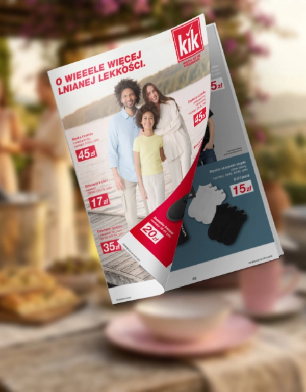 Unoszący się katalog KiK z rodzinnym zdjęciem i cenami ubrań, na tle rozmytego stołu ogrodowego z kwiatami i kubkiem.