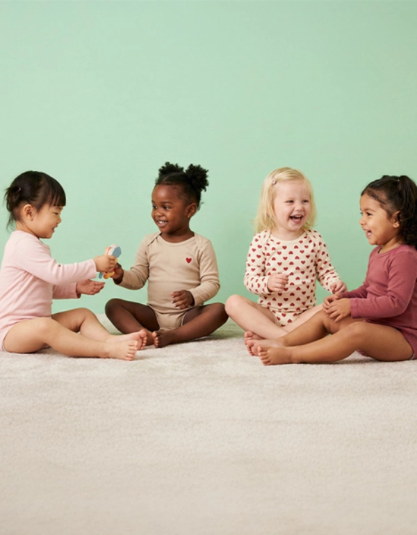 Czworo dzieci siedzących na jasnym dywanie, zaangażowanych w zabawową wymianę zdań, ubranych w kolorowe piżamy na tle delikatnej zieleni.