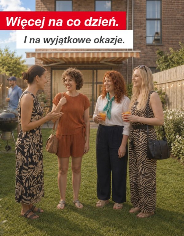 Grupa osób rozmawia i pije napoje w ogrodzie na tyłach domu z drewnianym ogrodzeniem i girlandami świetlnymi.