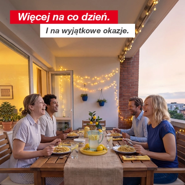 Cztery osoby spędzają wieczorny posiłek, jedząc makaron i pijąc lemoniadę na udekorowanym balkonie z girlandami świetlnymi i roślinami w doniczkach.