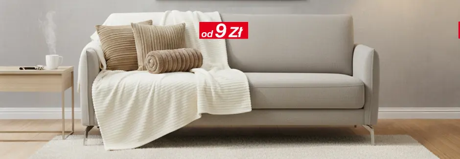 Jasny salon z szarą sofą, poduszkami i kocem, stolikiem i lampą stojącą.