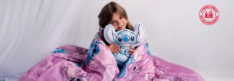 Dziecko owinięte różowym kocem z motywem Stitcha, trzymające pluszową zabawkę Stitch, siedzi na miękkim białym tle.