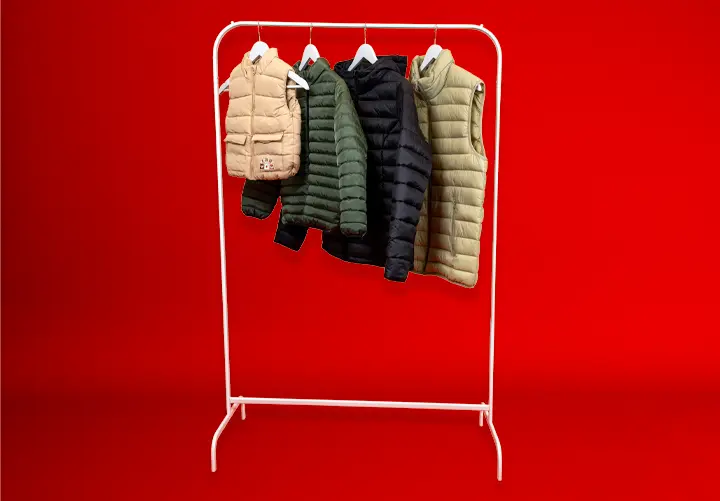 Biały wieszak prezentuje cztery pikowane kamizelki w różnych kolorach: beżowym, ciemnozielonym, granatowym i oliwkowym na tle czerwonym. Biały wieszak prezentuje cztery pikowane kamizelki w różnych kolorach: beżowym, ciemnozielonym, granatowym i oliwkowym na tle czerwonym.