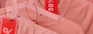 Zbliżenie na różowe ubrania z czerwonymi napisami „50%” na białych wieszakach.
