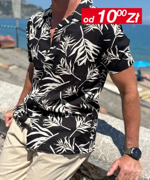 Mężczyzna w swobodnej pozie, ubrany w zielony T-shirt i jasnoniebieskie szorty, w czarnych butach sportowych, na tle miękkiego tła.