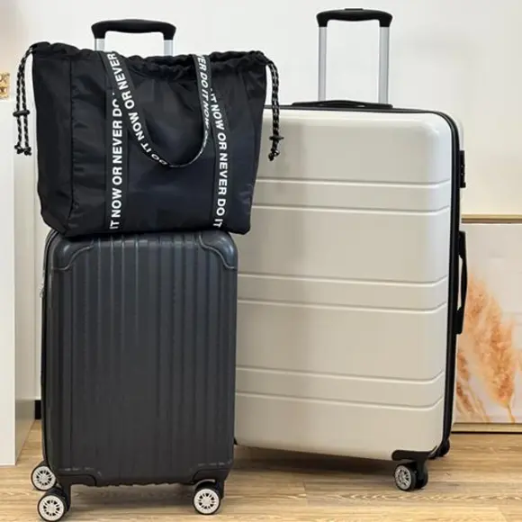 Czarna torba ze sznurkiem znajduje się na szczycie czarno-srebrnej walizki, ułożonej obok białej walizki w stylowej konfiguracji podróżnej.