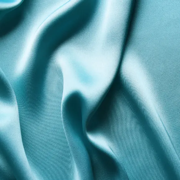 Zbliżenie na turkusową tkaninę satynową, która połyskuje w świetle.