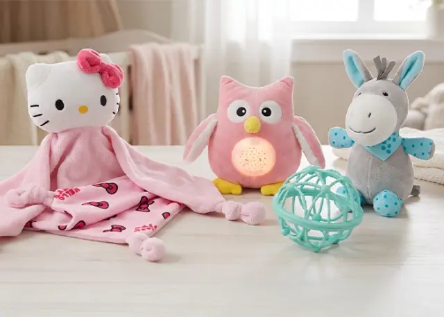 Przytulna kolekcja pluszowych zabawek: koc Hello Kitty, różowa sowa, szary osiołek i turkusowa piłka na sprężystej powierzchni z jasnego drewna.
