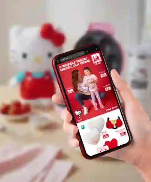 Ręka trzyma smartfon, na którym widoczna jest reklama Hello Kitty, w tle widać pluszową zabawkę Hello Kitty, przekąski i gofrownicę.