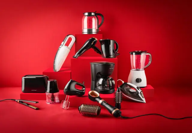 Zestaw różnych urządzeń domowych, w tym czajnika, blendera, ekspresu do kawy i odkurzacza, ułożonych na czerwonych stopniach.
