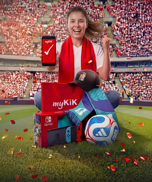 Osoba na stadionie trzyma smartfon z aplikacją myKiK, otoczona konsolą Nintendo Switch, piłką nożną, czapką, szalikiem i paczką myKiK.