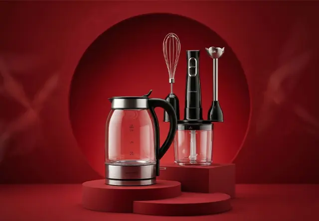 Elektryczny czajnik szklany oraz czarny blender ręczny z końcówką trzepaczki i rozdrabniacza stoją na czerwonych, okrągłych podestach na czerwonym tle.