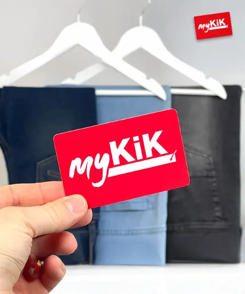 Ręka trzyma czerwoną kartę lojalnościową myKiK przed wiszącymi dżinsami w różnych odcieniach.