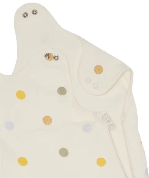 Zbliżenie na kremową odzież dla niemowląt w wielobarwne groszki, z zatrzaskowymi guzikami i zamkiem błyskawicznym z boku.