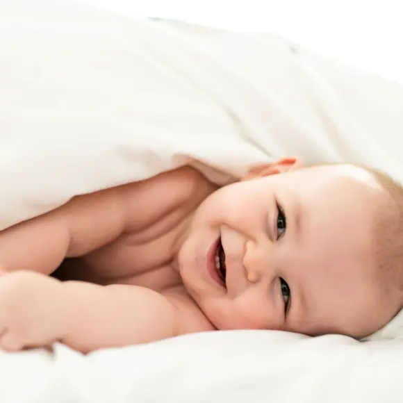 Uśmiechnięte dziecko leży w łóżeczku z białymi prześcieradłami.