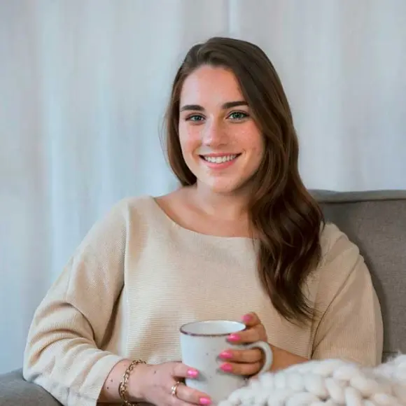 Kobieta siedzi na sofie i trzyma filiżankę kawy.