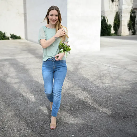 Osoba w pasiastej koszuli i białych spodniach trzyma kosz kolorowych kwiatów.