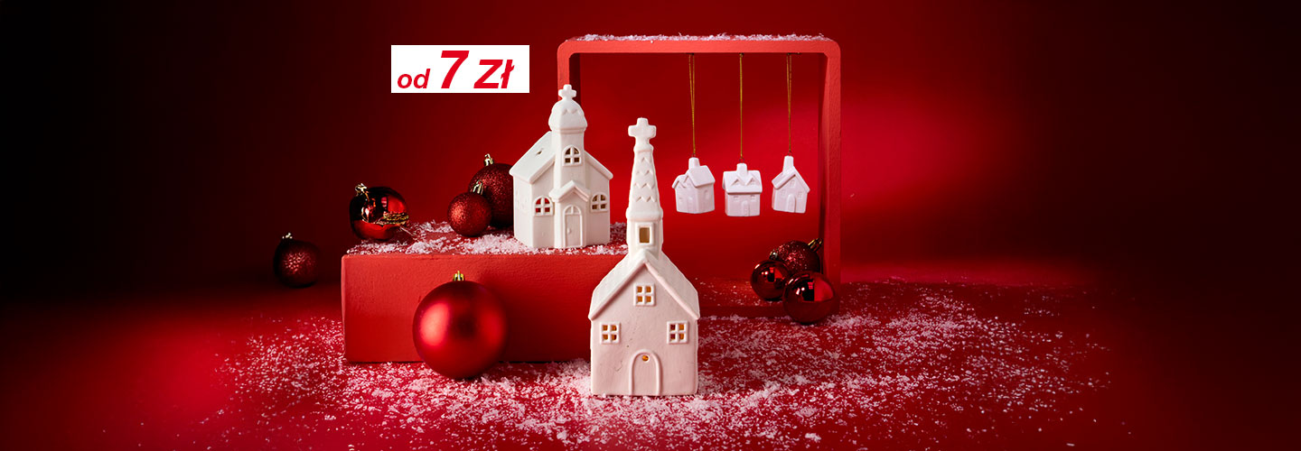 Białe ceramiczne domki i ozdoby na czerwonym tle, pokryte dekoracjami przypominającymi śnieg, tworzą świąteczną atmosferę.