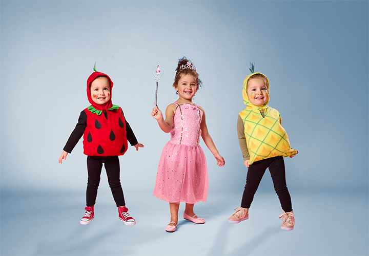 Trójka dzieci w zabawnych owocowych kostiumach: truskawka, ananas i księżniczka w różowej sukience.