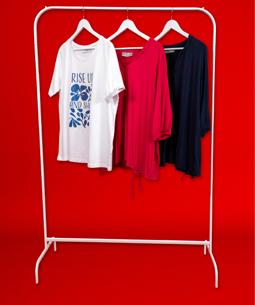 Trzy stylowe koszule na białym wieszaku: biały T-shirt z nadrukiem, różowa bluzka i granatowy top na tle intensywnie czerwonym.