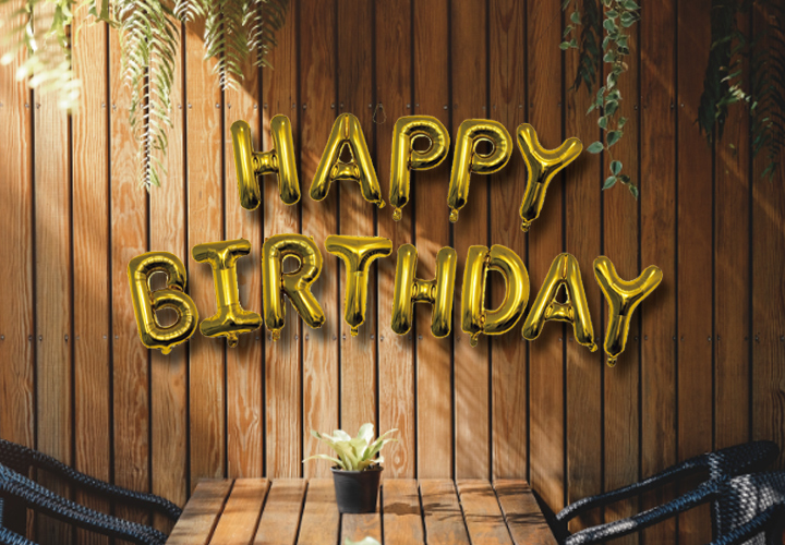 Złote balony z napisem „Happy Birthday” na tle drewnianej ściany.